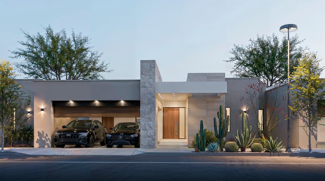 Fachada del Modelo A al anochecer: una sola planta, cochera techada con dos autos y jardín de cactáceas y agaves.
